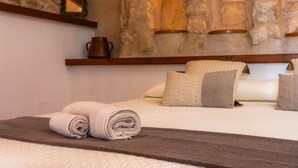 Una cama bien tendida con una colcha marrón, una toalla enrollada y una pared de piedra con iluminación empotrada.