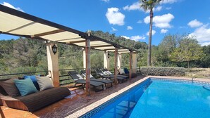 Zona de piscina con sillones de descanso, un área de estar techada y vistas del paisaje circundante.