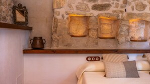 Una pared de piedra con un estante que sostiene una maceta, un espejo enmarcado y luces fijadas a la pared.