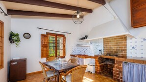 Une cuisine avec un four en briques, des chaises en bois, une table à manger et un luminaire suspendu.