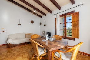 Un coin repas comprenant une table en bois, des chaises en osier, un canapé et une fenêtre avec des volets en bois.