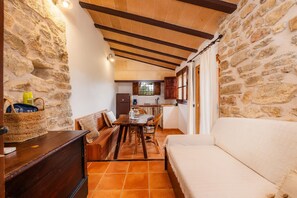 A rustic room with stone walls, a wooden ceiling, a dining area with a table and chairs, and a sofa.