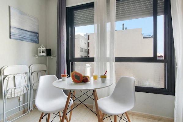 A room with a round table, two white chairs, a fruit bowl, a glass pitcher, and a white lantern on a shelf.
