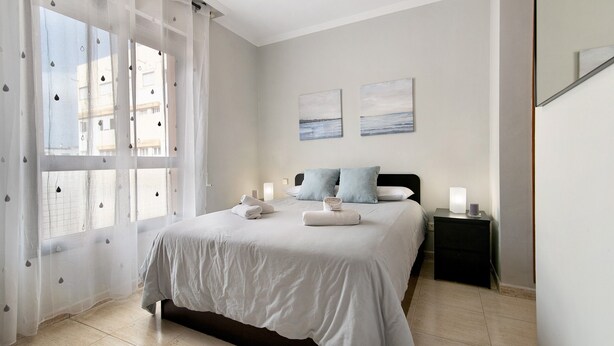 A bedroom with a bed, two pillows, a nightstand, and a window with sheer curtains. - Vacation Home "Laura y Juan" with Sea View & Wi-Fi (Las Palmas de Gran canaria)