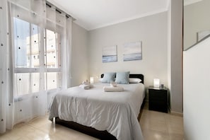 A bedroom with a bed, two pillows, a nightstand, and a window with sheer curtains.