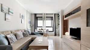A modern living room with a sofa, a coffee table, a TV, and a dining area with chairs and a table. - Vacation Home "Laura y Juan" with Sea View & Wi-Fi (Las Palmas de Gran canaria)