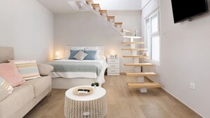 A modern bedroom with a bed, a sofa, a TV, a staircase, and a window.