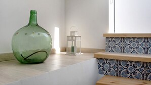 A green glass vase on a wooden shelf, a white lantern, and patterned tiles on the wall.