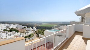 A rooftop terrace with a pool, white buildings in the background, and a clear sky.
