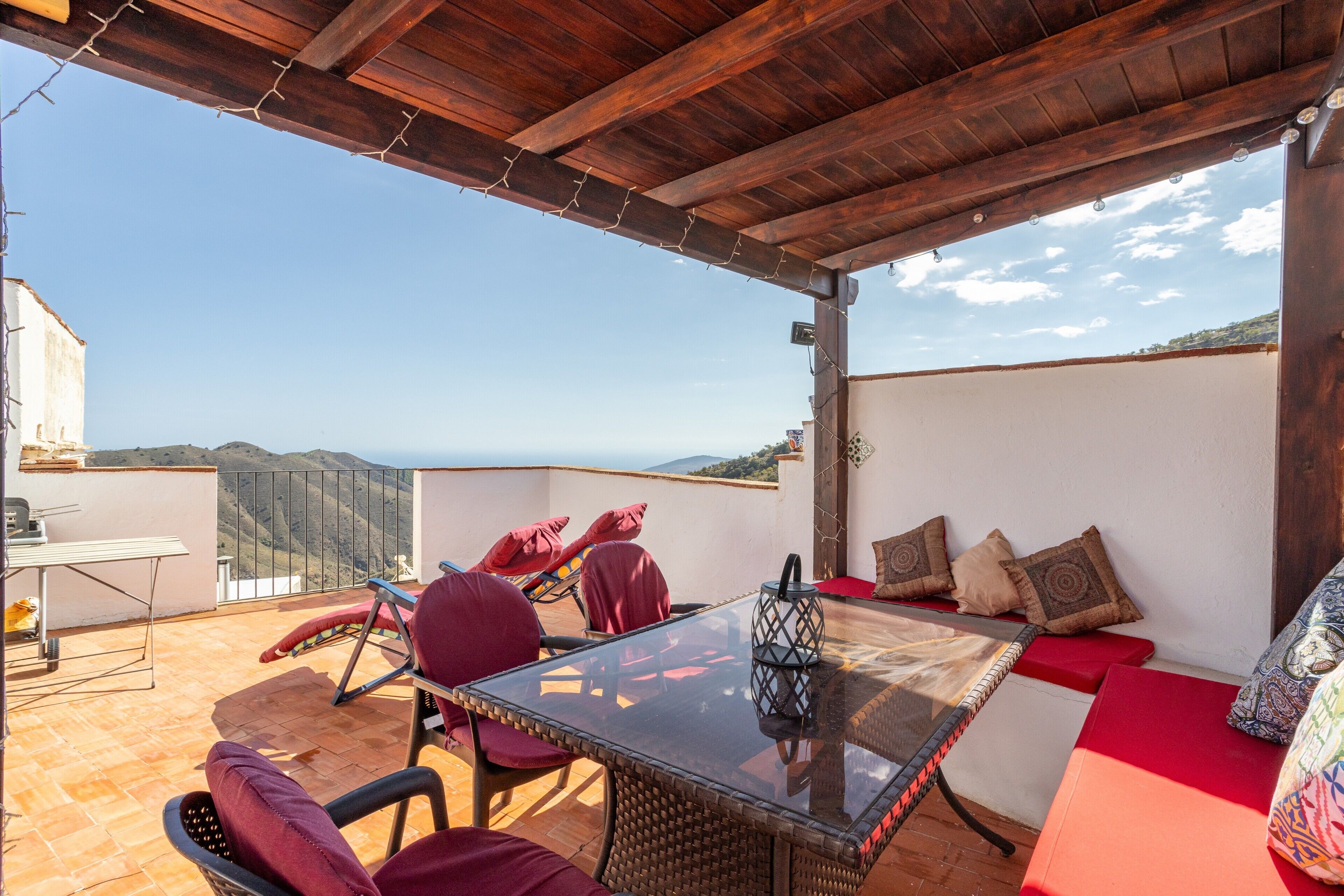 Un área de estar al aire libre techada con mesa y sillas, vista al paisaje y una estructura de pérgola.