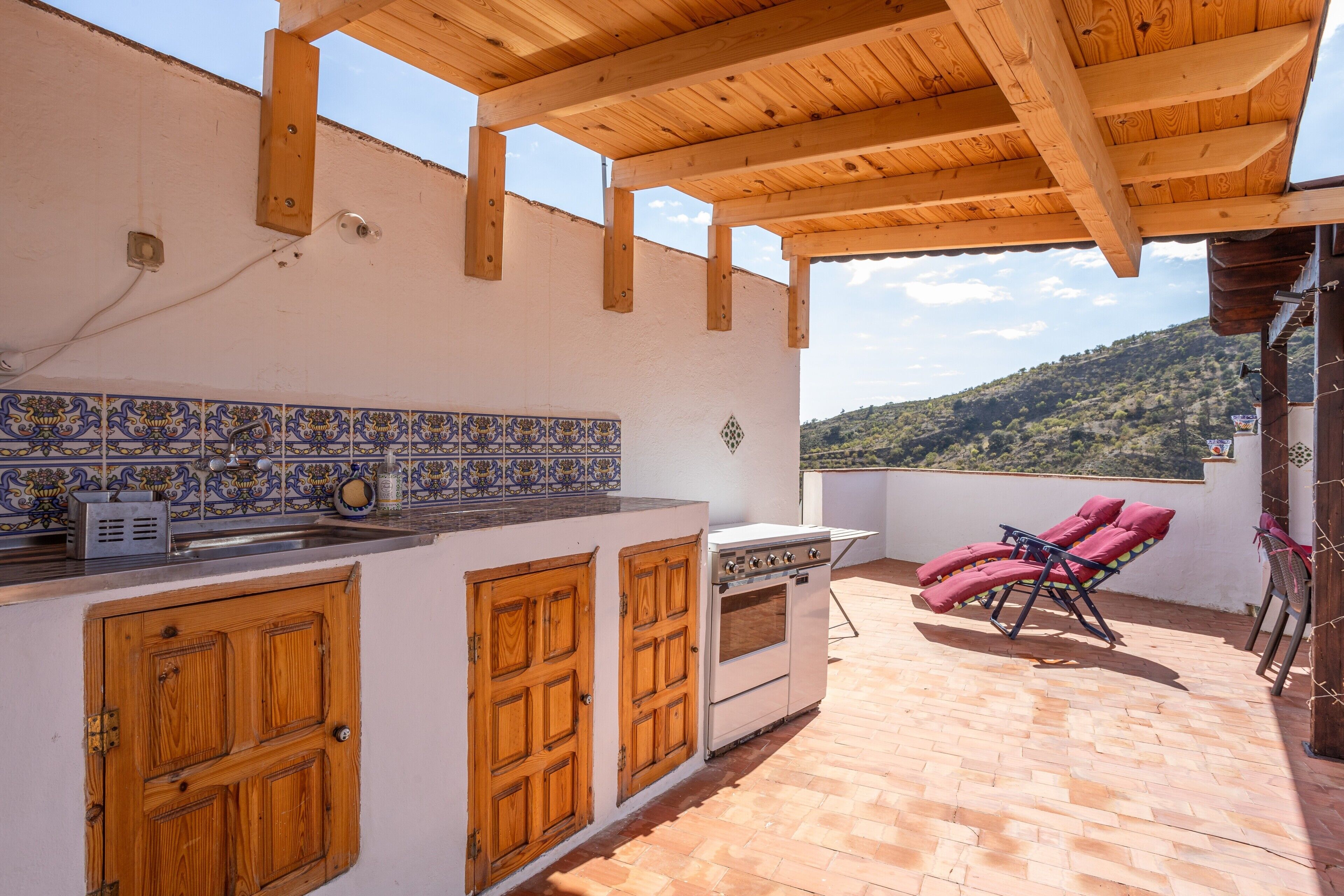 An outdoor kitchen with a tiled backsplash, wooden cabinets, and a gas stove.