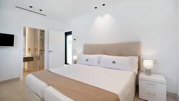 Een moderne slaapkamer met een groot bed, nachtkastjes, een televisie, en een zichtbare badkamer door een geopende deur.