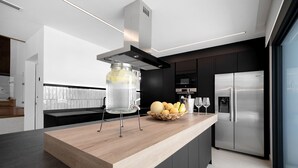 A modern kitchen with a wooden countertop, a stainless steel refrigerator, and a glass container on the island. - "Alba Sea" Villa with Private Pool, 2 Private Terraces and Wi-Fi (Chiclana de la Frontera)