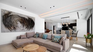 A modern living room with a sectional sofa, two round wooden tables, and a large abstract painting on the wall. - "Alba Sea" Villa with Private Pool, 2 Private Terraces and Wi-Fi (Chiclana de la Frontera)
