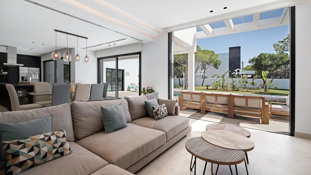 A modern living room with a sofa, a dining table, and a view of the outdoors. - "Alba Sea" Villa with Private Pool, 2 Private Terraces and Wi-Fi (Chiclana de la Frontera)