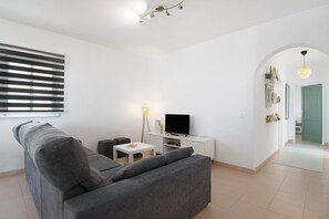 A modern living room with a grey sofa, a TV on a white stand, a small table, and a lamp. - Vacation Apartment 'Los Alisios Del Patron' with Mountain View, Private Terrace and Wi-Fi (Playa Honda)