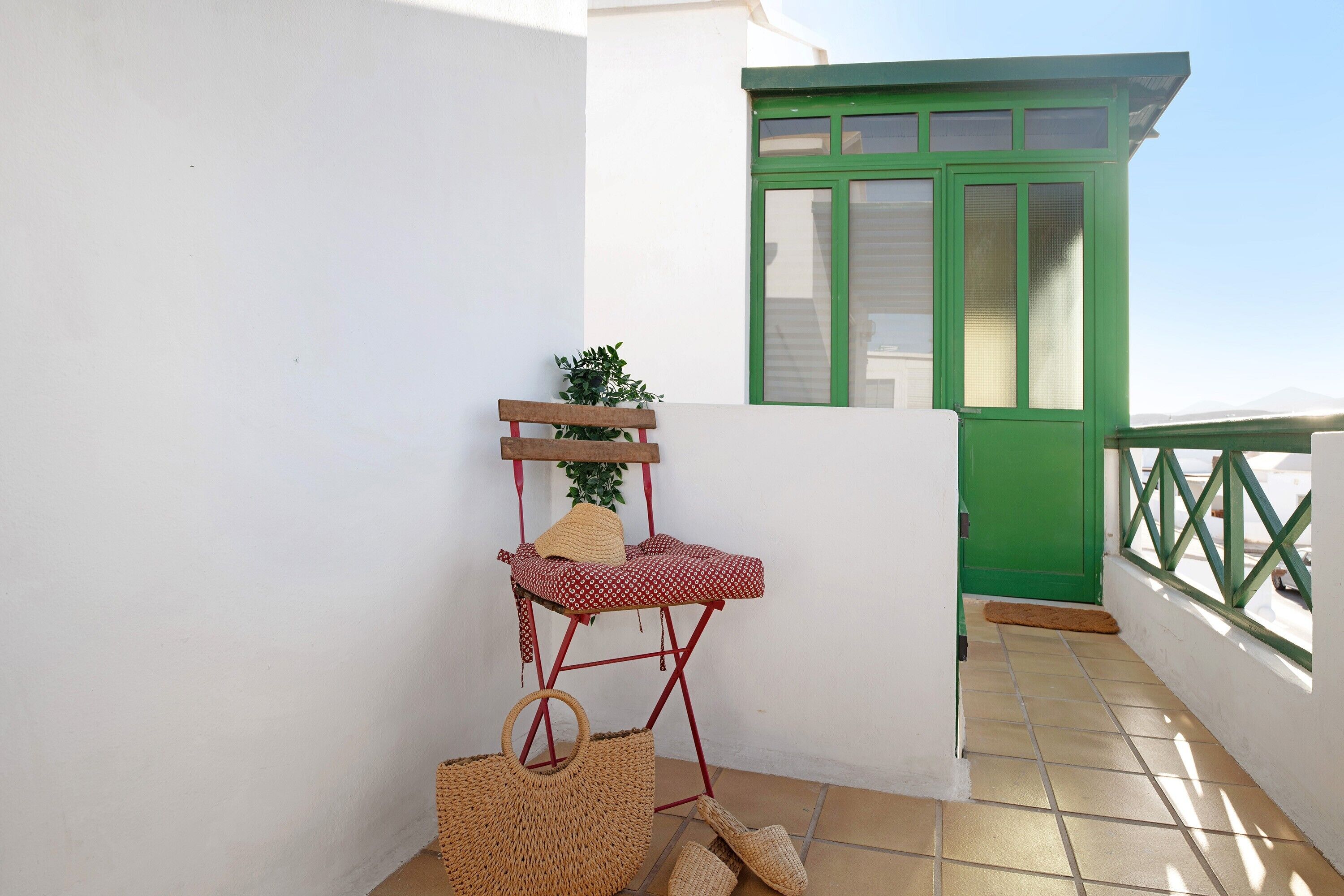 A balcony with a red and white chair, a woven basket, and a green door.