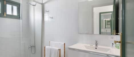 Un baño moderno con ducha envuelta en vidrio, un lavabo blanco y un espejo grande.