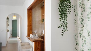 Un pasillo con un banco de madera, una puerta verde y una zona de cocina con una planta colgante.