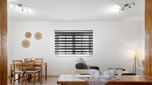 Un comedor con mesa y sillas de madera, una ventana con persianas y una lámpara.