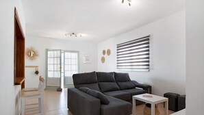 Una sala moderna con un sofá modular, una mesita, una silla y un ventanal con persianas.