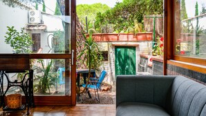 A living room with a sofa, a table with a basket, and a view of a garden with cacti and a green door.