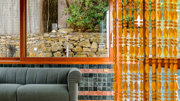 A room with a stone wall, a wooden bench, and a window with a view of a stone wall and greenery.