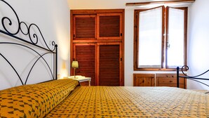 A bedroom with a bed, a wooden wardrobe, a desk, and a window.