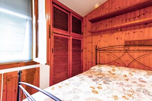 Une chambre à coucher avec un lit, des murs en bois, une fenêtre avec des stores et une tête de lit en métal.