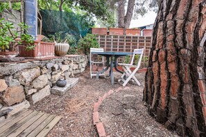 Une terrasse avec une table et des chaises, entourée de plantes en pot et d’un mur de pierre.