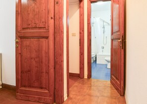 Un couloir avec des portes en bois menant à une salle de bain équipée d’une douche, de toilettes et d’un lavabo.