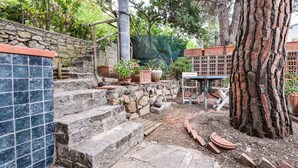 A stone staircase leading to a terrace with potted plants, a metal table, and a tree trunk.