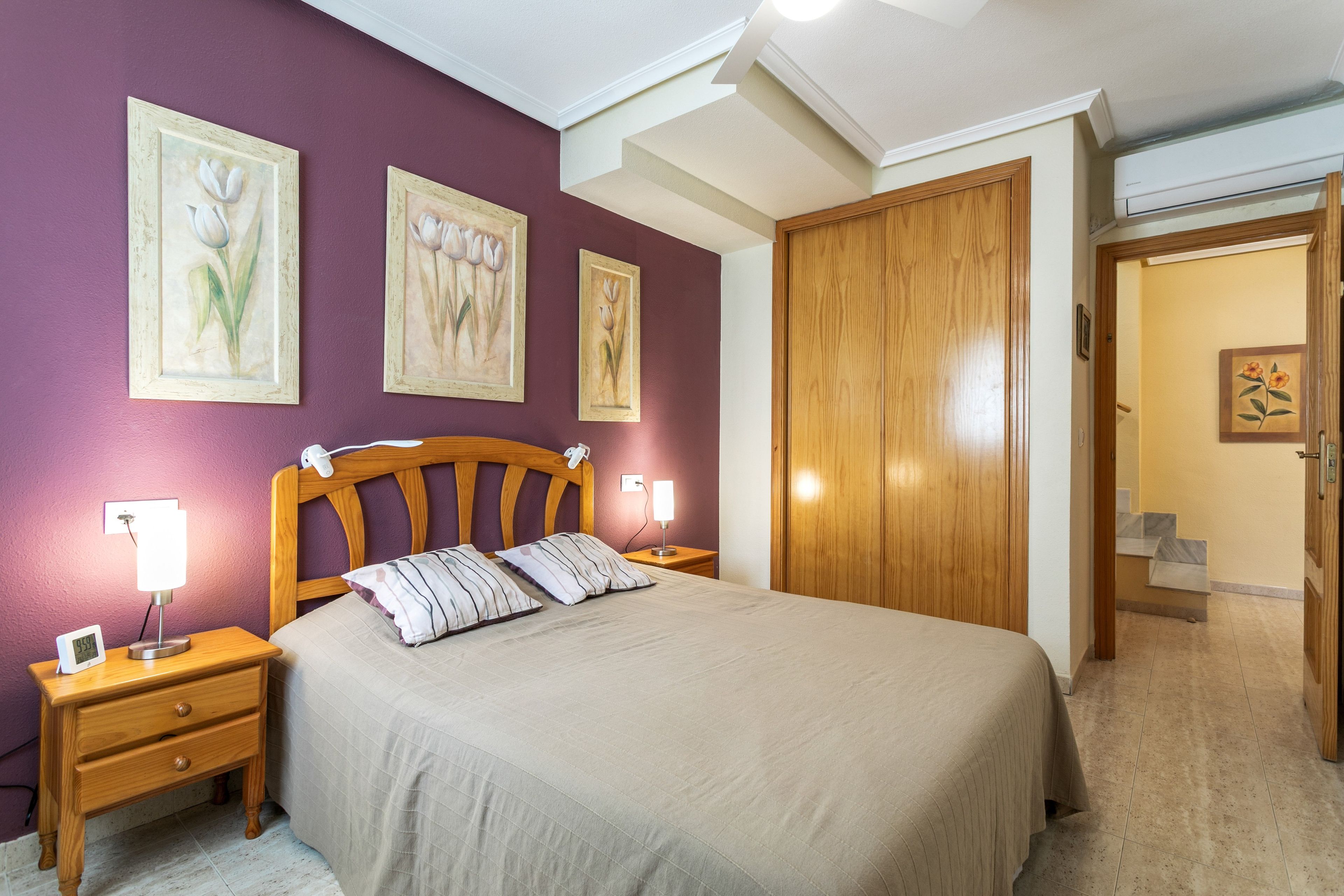 Un dormitorio con cama, mesitas de noche, un armario junto a la cama y un guardarropa de madera.