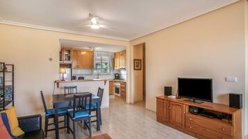 Un espacio habitable compacto con comedor, kitchenette y televisor sobre un mueble de madera.