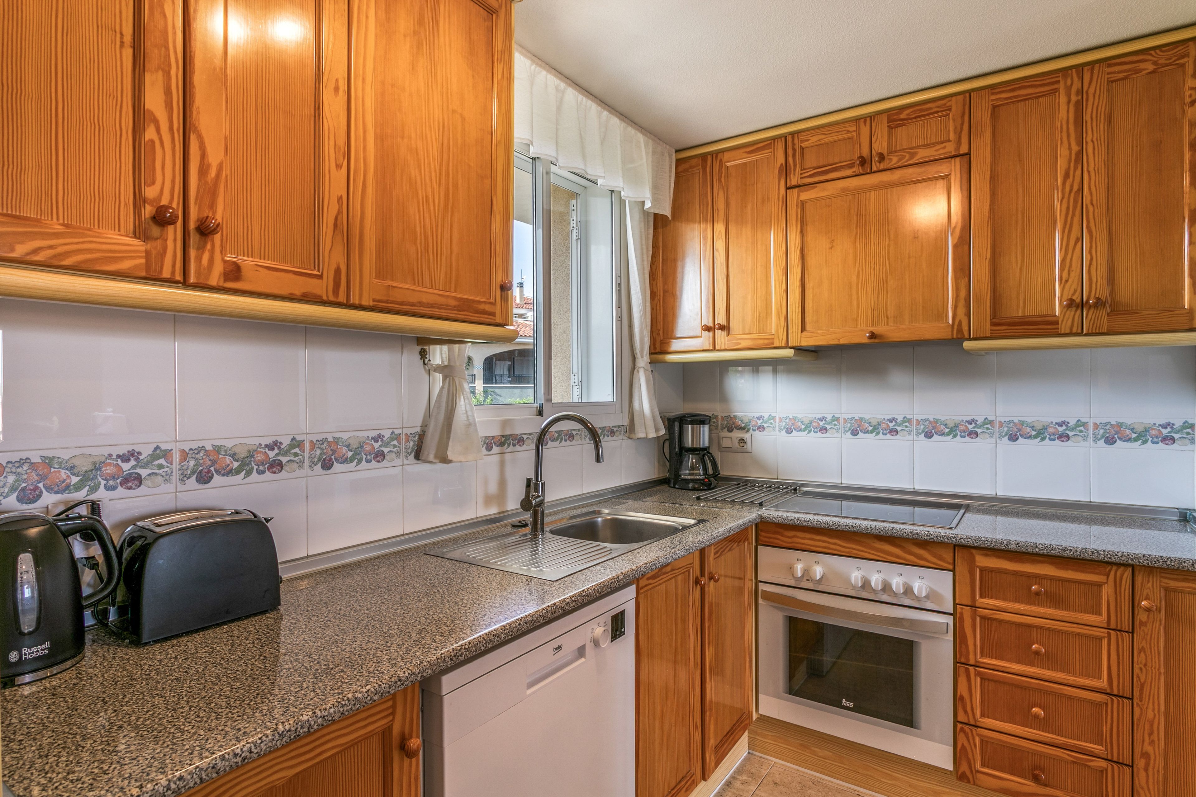 A kitchen with wooden cabinets, a stainless steel sink, a coffee maker, a toaster, and a dishwasher.