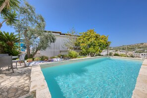 A swimming pool with stone tiles, surrounded by potted plants and outdoor furniture.