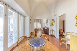 A spacious room with a dining table, chairs, a sofa, and a window with blinds.
