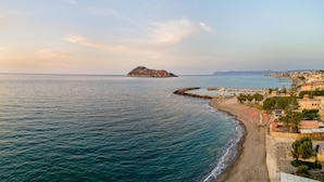 A coastal view with a rocky island, a beach with umbrellas, and a pier extending into the sea. - Platanias Beachfront Villa Elsa-90m To Main Square (Platanias)