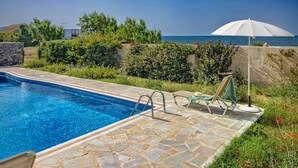 A swimming pool with stone tiles, a lounge chair, and an umbrella. - Platanias Beachfront Villa Elsa-90m To Main Square (Platanias)