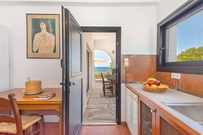 Cozinha com área de refeições e vista para o mar, com uma cesta de frutas no balcão.