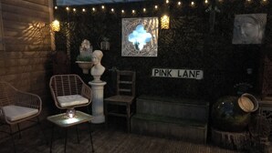 A cozy outdoor seating area with wicker chairs and a white table, a decorative bust, and a sign reading "PINK LANF".