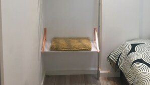 A room with a white wardrobe, a wooden hanger rack, a folded towel, and a bed with a patterned blanket.