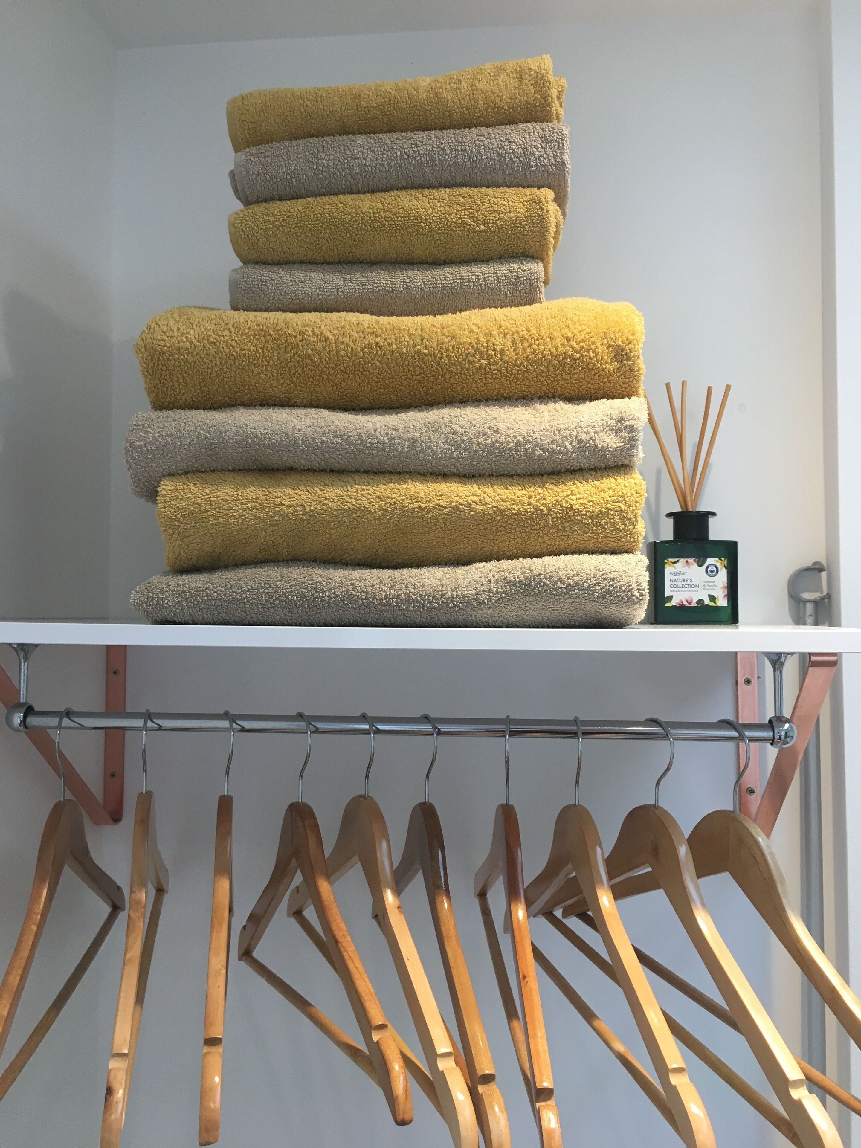 A stack of towels in yellow and gray colors on a shelf, with a small bottle of reed diffuser next to them.