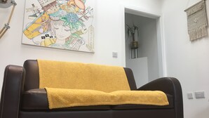 A modern living room with a dark brown leather sofa, a yellow throw blanket, and a colorful abstract painting on the wall.