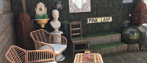 A patio area with wicker furniture, a small table, and decorative items against a wall with a 'PINK LANDF' sign.