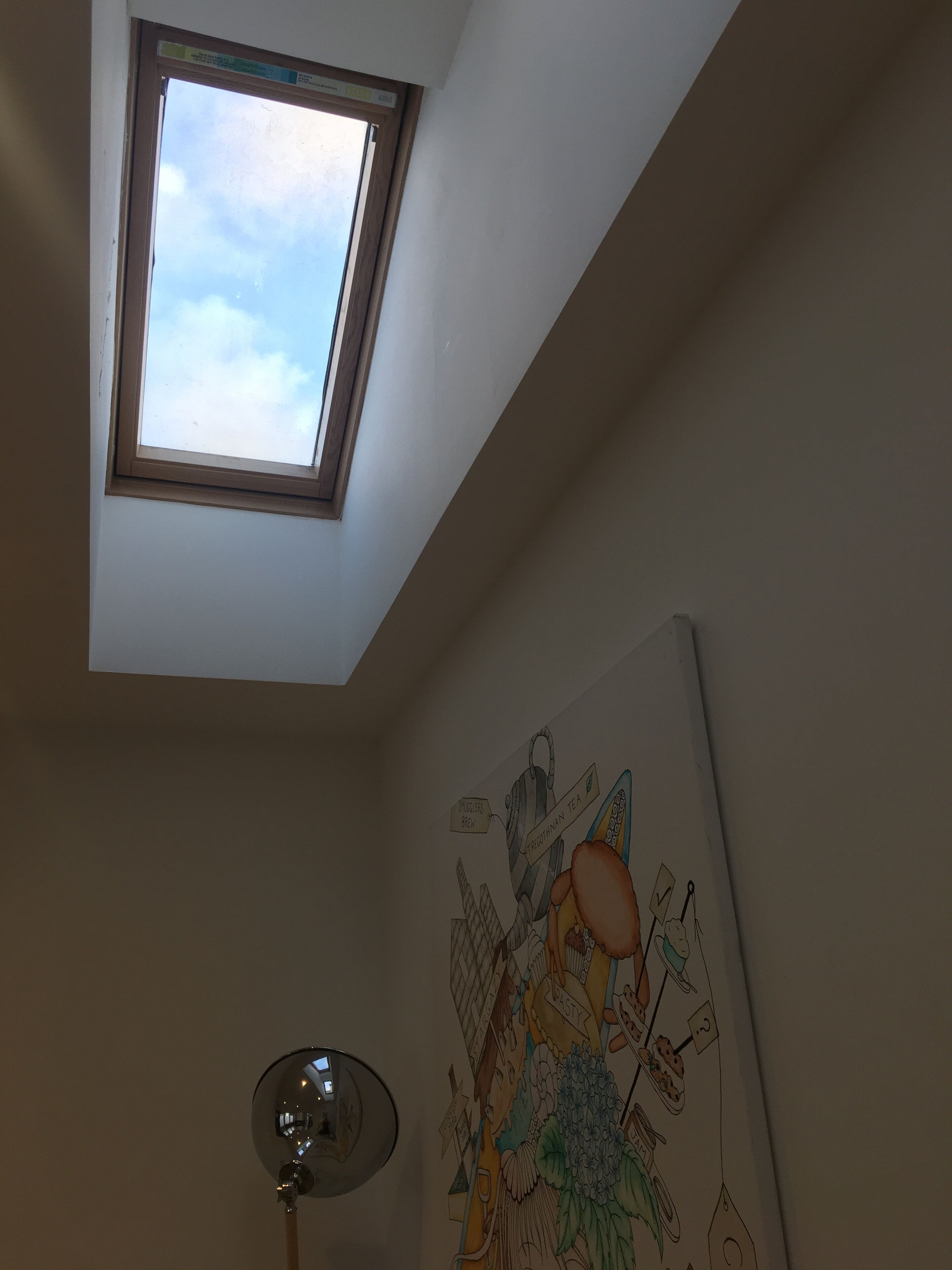 Ett takfönster, en vägg med en färgstark väggmålning och en golvlampa.