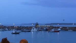 A marina with boats docked, a building with a dome structure, and a calm water body.