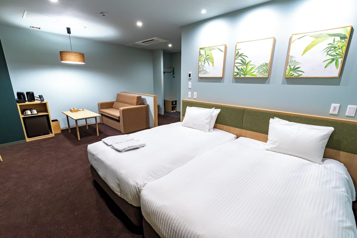 A hotel room with two beds, a sofa, a coffee station, and wall art.