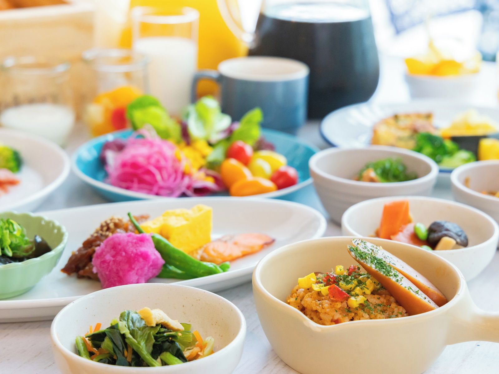 A variety of dishes on a table, including bowls of food and plates with colorful vegetables.