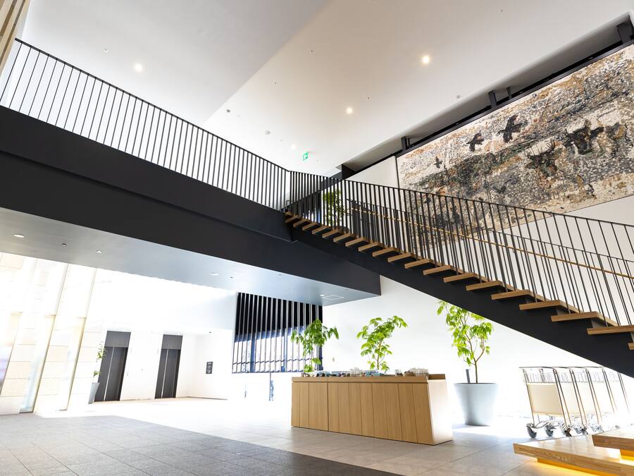 A spacious lobby with a modern staircase, a reception desk, and large windows allowing natural light.